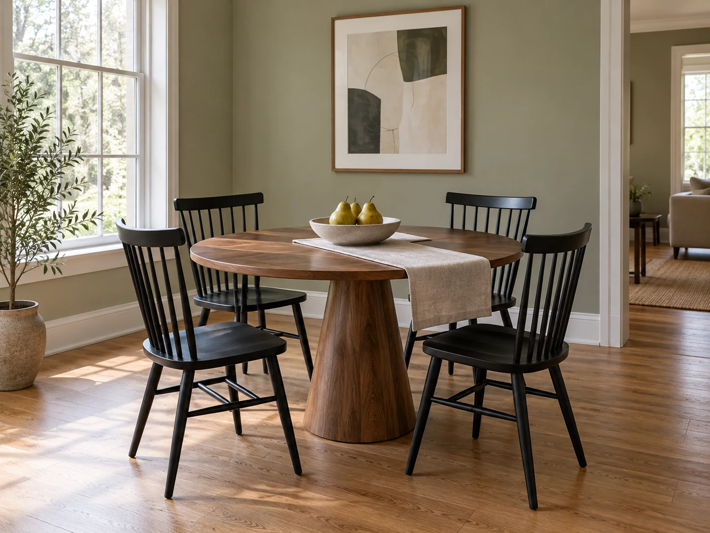 Round walnut dining table with black spindle chairs in a sage green dining nook